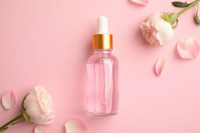 Flat lay composition with rose essential oil and flowers on pink background