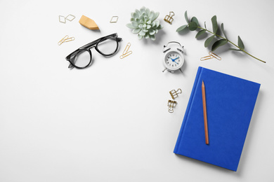 Photo of Glasses, alarm clock, eucalyptus and different stationery on white background, top view. Classic blue - color of the Year 2020