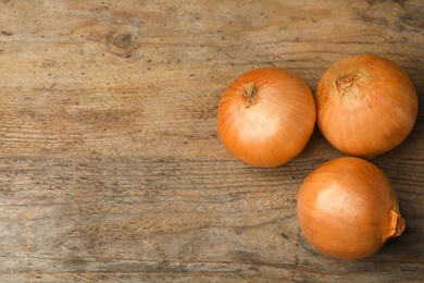Photo of Ripe onions on rustic wooden table, flat lay with space for text