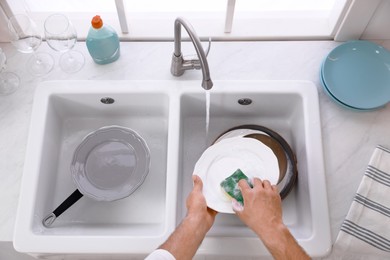 Man washing plate above sink in kitchen, closeup