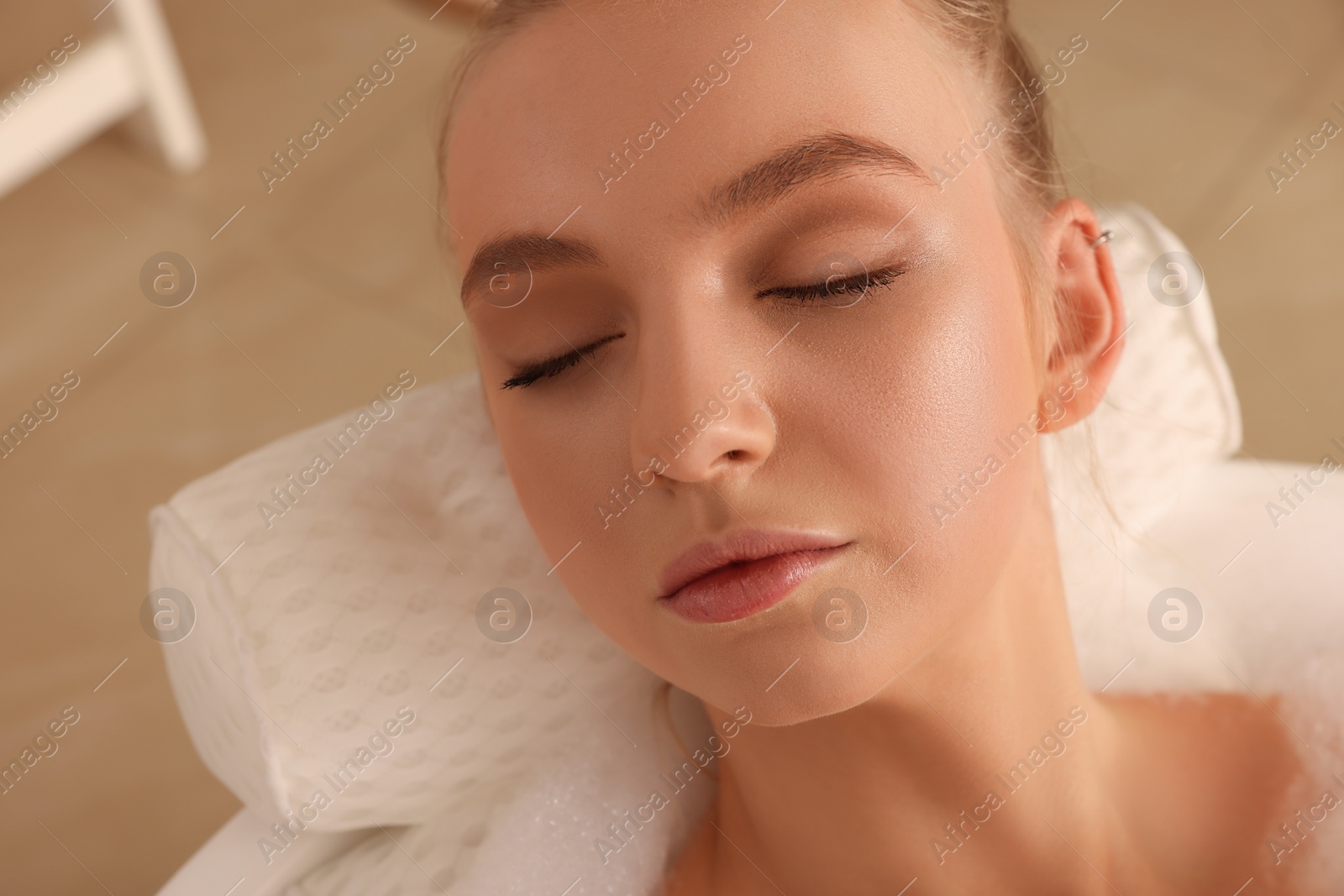 Photo of Young woman using pillow while enjoying bubble bath indoors, closeup