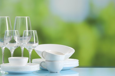 Photo of Set of many clean dishware and glasses on light blue table against blurred green background. Space for text