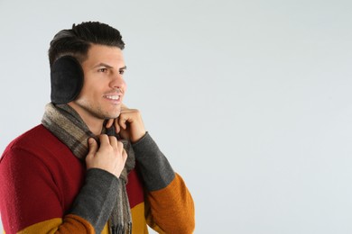 Photo of Man wearing stylish earmuffs and scarf on light background. Space for text