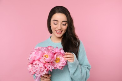 Beautiful young woman with bouquet of peonies on pink background