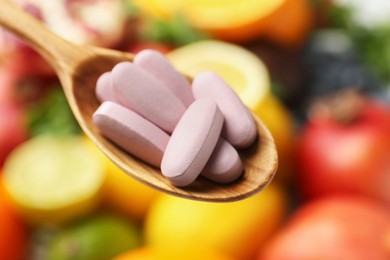 Photo of Vitamin pills in spoon against fresh fruits, closeup