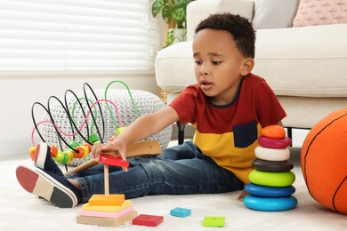 Photo of Cute African-American boy playing with colorful toys on floor at home
