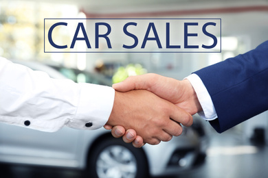 Young salesman shaking hands with client in car dealership, closeup