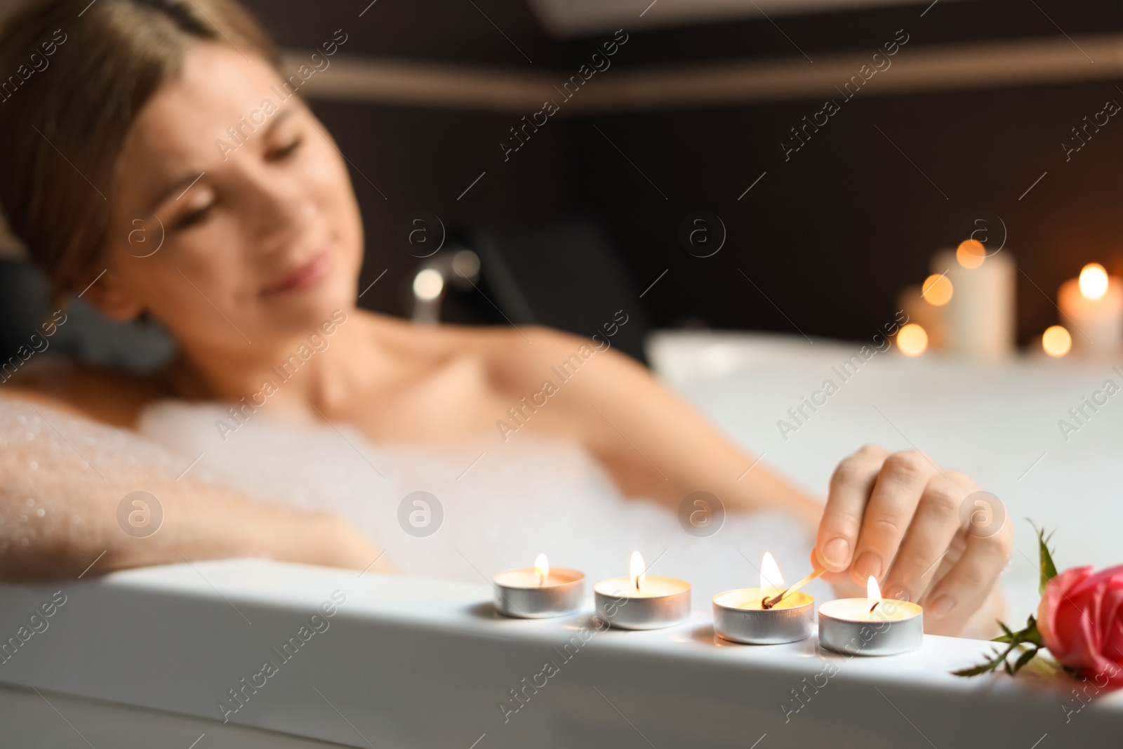 Photo of Beautiful woman lighting candles while taking bubble bath, focus on hand. Romantic atmosphere