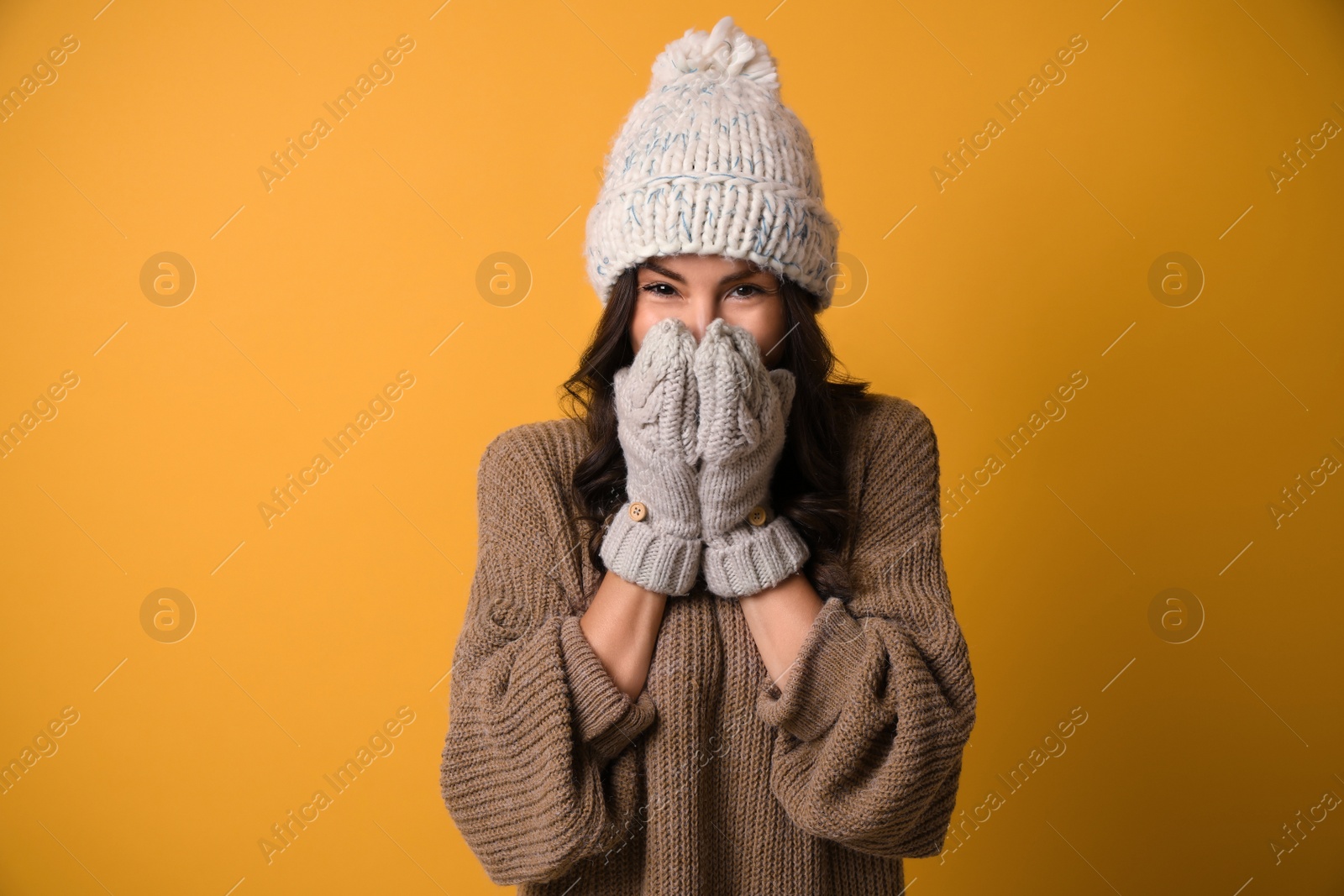 Photo of Young woman in warm sweater, hat and mittens on yellow background. Christmas season