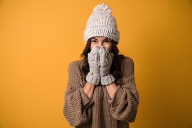 Young woman in warm sweater, hat and mittens on yellow background. Christmas season