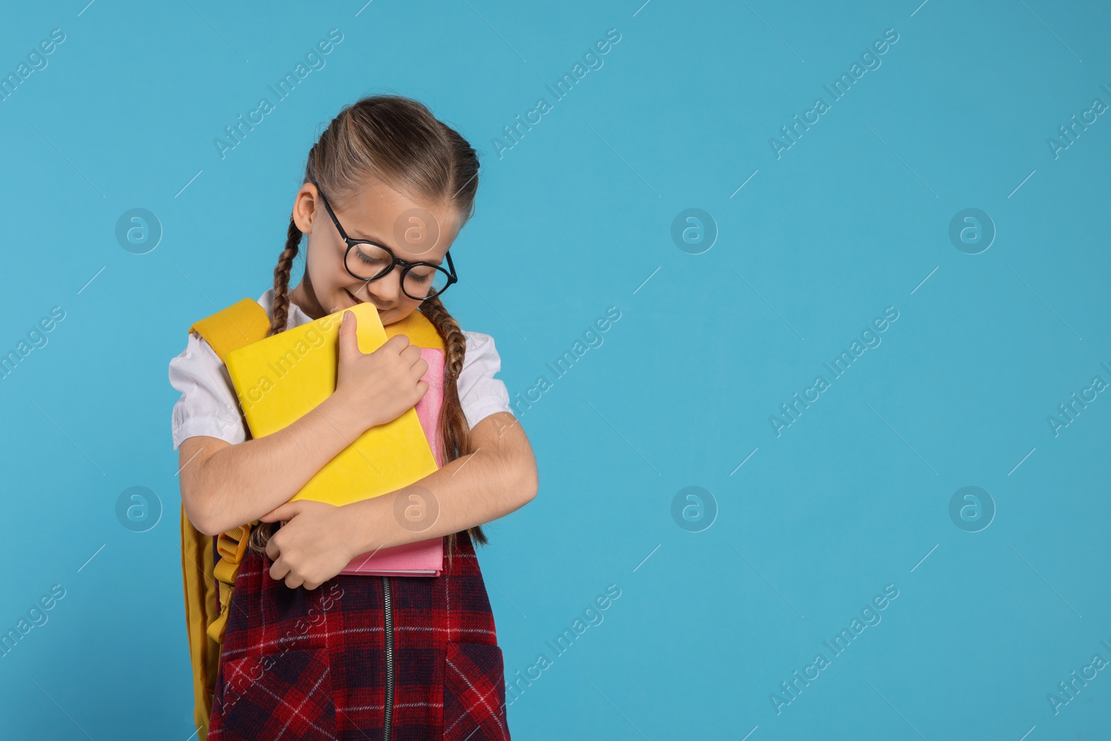 Photo of Happy schoolgirl in glasses with backpack and books on light blue background, space for text