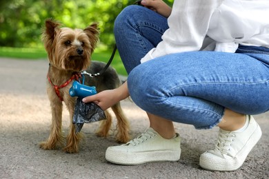 Photo of Woman with cute dog taking waste bag from holder in park, closeup