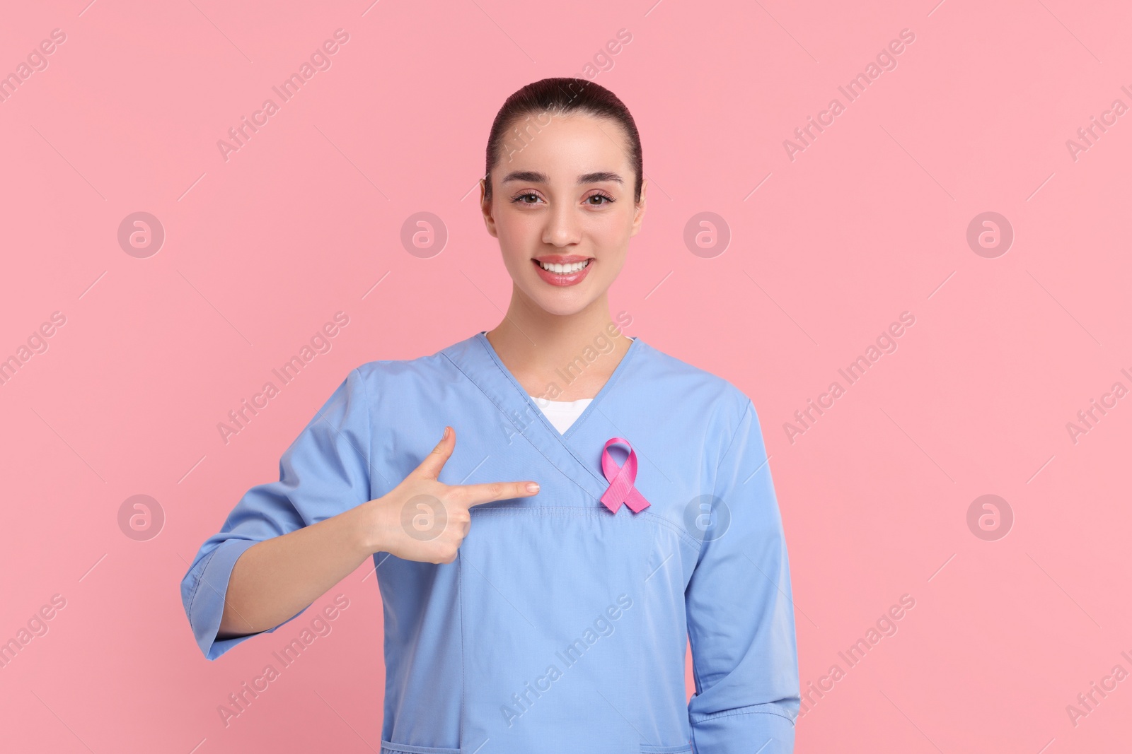 Photo of Mammologist pointing at pink ribbon on color background. Breast cancer awareness