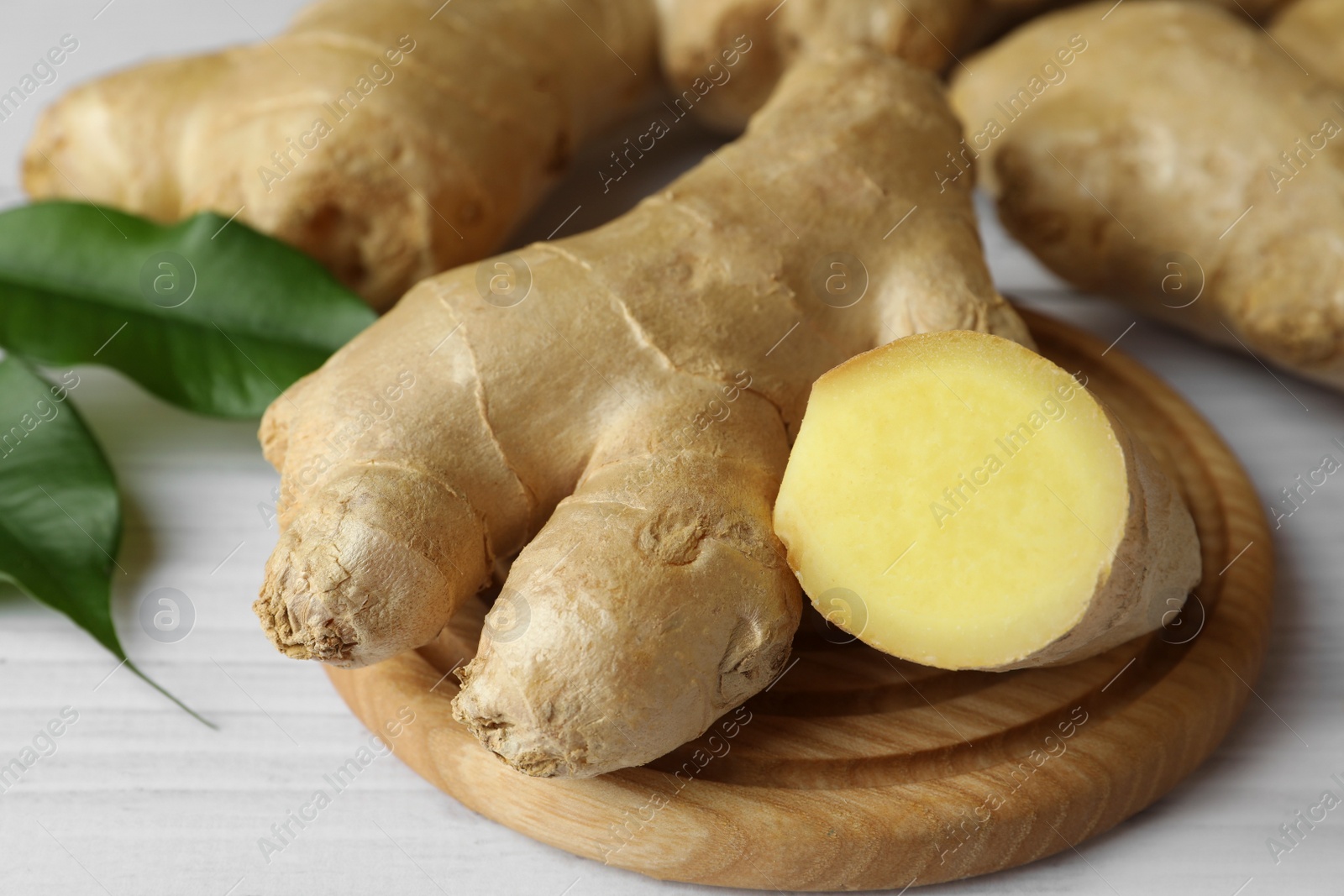 Photo of Fresh ginger with leaves on white wooden table, closeup