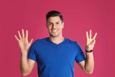 Photo of Man showing number eight with his hands on pink background