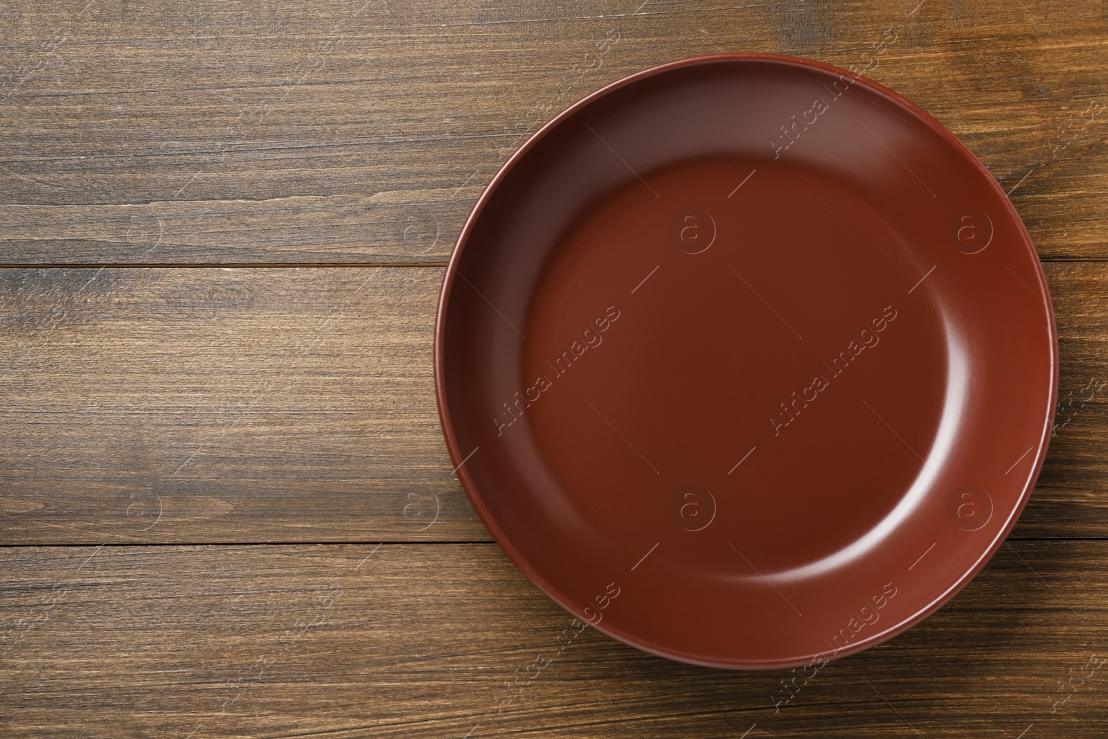 Photo of Empty brown ceramic plate on wooden table, top view. Space for text