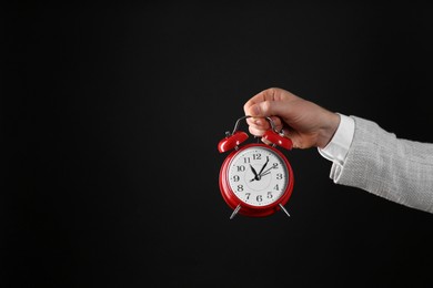 Closeup view of businessman holding alarm clock on black background, space for text. Time management