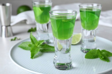 Photo of Delicious mint liqueur with lime and green leaves on white table, closeup