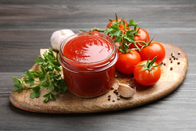 Photo of Tasty ketchup, fresh tomatoes, parsley and spices on grey wooden table