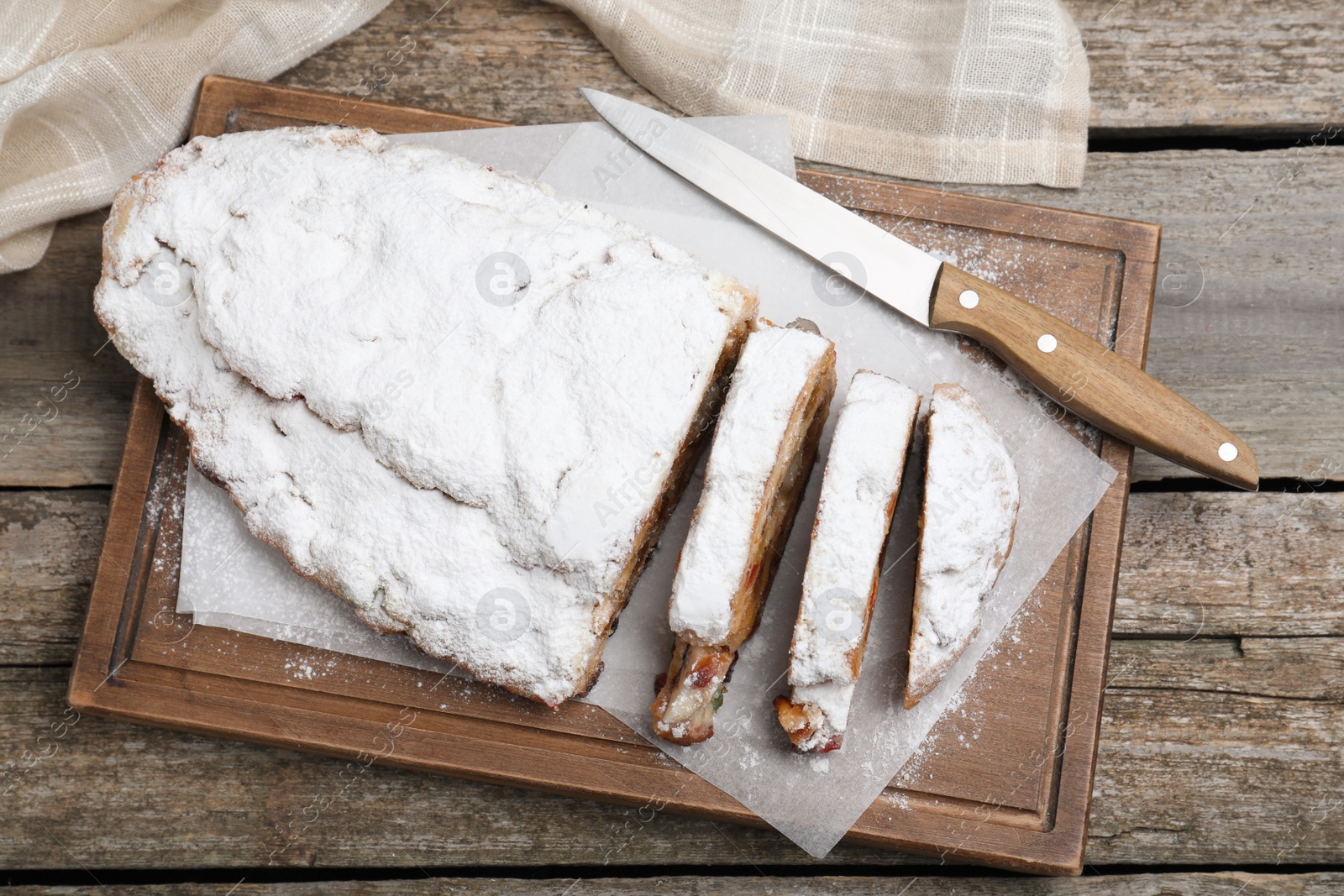 Photo of Traditional Christmas Stollen with icing sugar on wooden table, top view