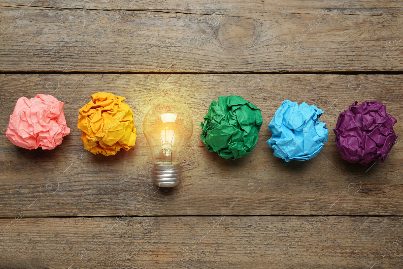 Photo of Creative flat lay composition with lightbulb and colorful paper balls on wooden table. Idea concept