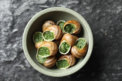 Delicious cooked snails in bowl on grey textured table, top view