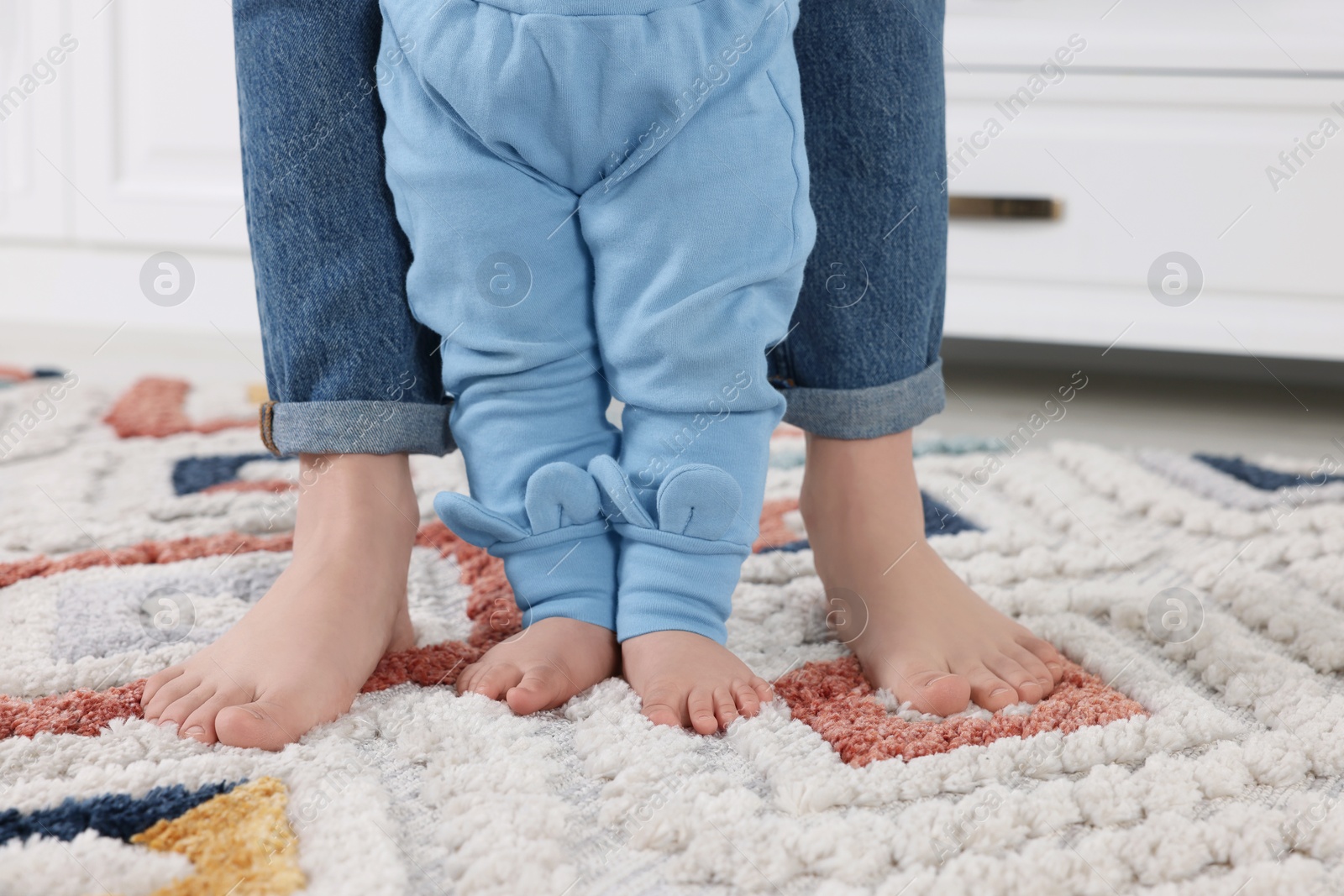 Photo of Mother supporting her baby son while he learning to walk on carpet indoors, closeup