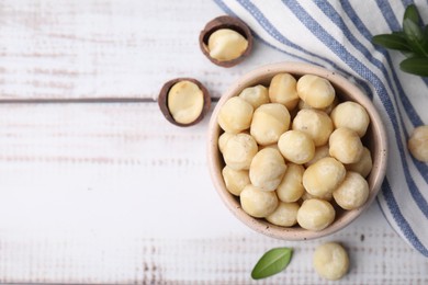 Photo of Tasty peeled Macadamia nuts in bowl on light table, flat lay. Space for text