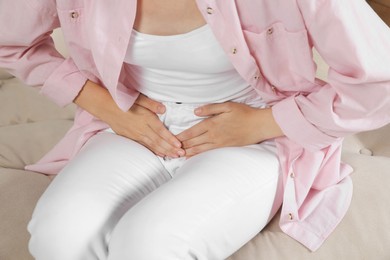 Woman suffering from cystitis on sofa at home, closeup