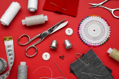 Photo of Flat lay composition with thimbles and different sewing tools on red background