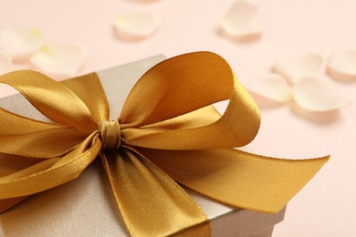 Beautiful gift box with golden bow on pink background, closeup