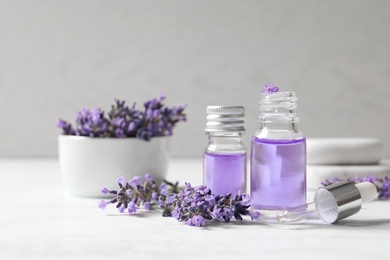 Photo of Glass bottles of natural cosmetic oil and lavender flowers on white wooden table