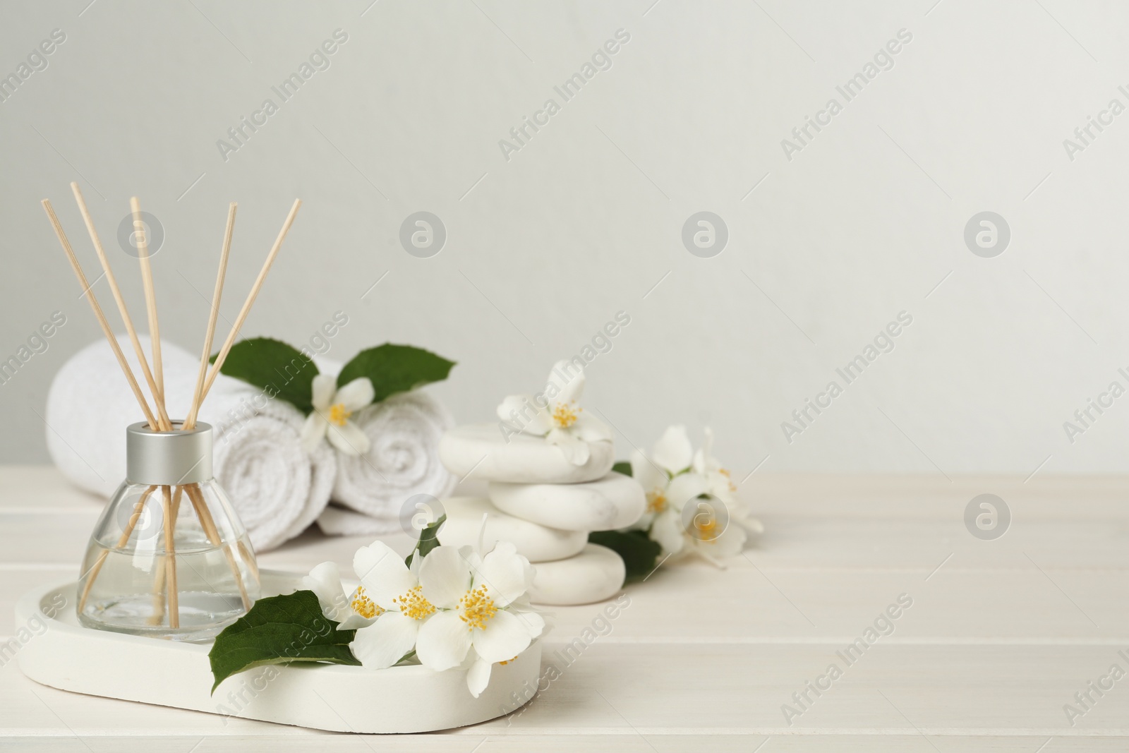 Photo of Air reed freshener and beautiful jasmine flowers on white wooden table, space for text