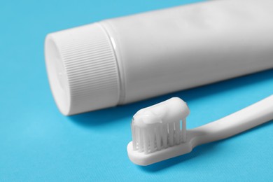 Photo of Plastic toothbrush with paste and tube on light blue background, closeup