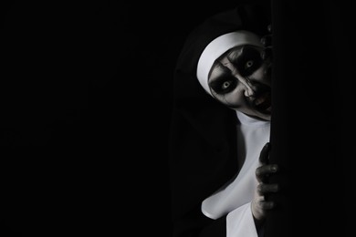 Photo of Scary devilish nun hiding on black background, space for text. Halloween party look