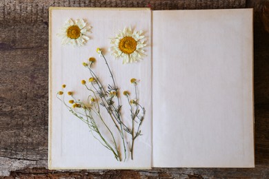 Photo of Open book with beautiful dried flowers on wooden table, top view