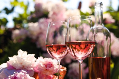 Photo of Bottle and glasses of rose wine near beautiful peonies in garden, closeup. Space for text