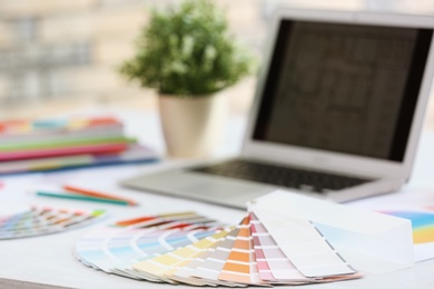 Paint color palette samples and laptop on table, closeup