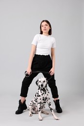 Beautiful young woman with her adorable Dalmatian dog on light grey background. Lovely pet