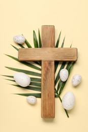 Wooden cross, painted Easter eggs and palm leaf on beige background, flat lay