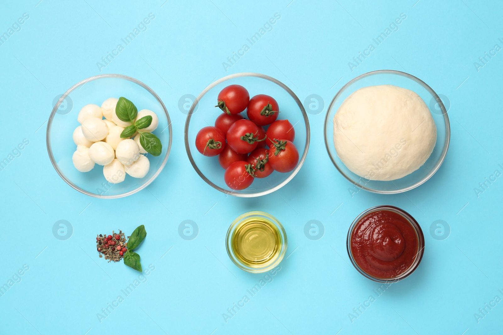 Photo of Raw dough and other ingredients for pizza on light blue background, flat lay