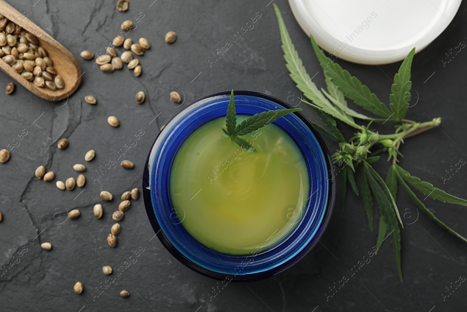 Photo of Jar of hemp cream and seeds on dark stone table, flat lay. Organic cosmetics
