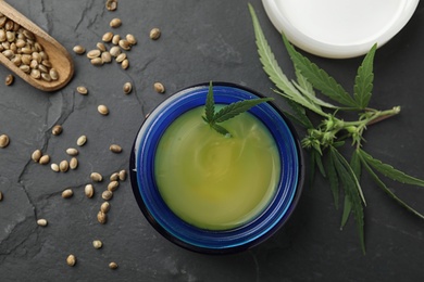 Photo of Jar of hemp cream and seeds on dark stone table, flat lay. Organic cosmetics