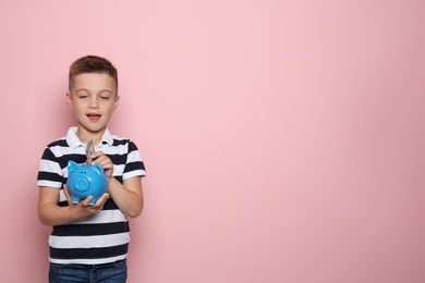Photo of Emotional little boy putting money into piggy bank on color background. Space for text