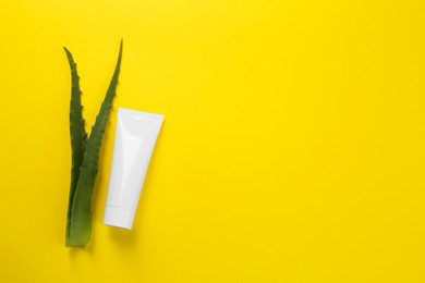 Photo of Aloe vera toothpaste in blank tube and green leaves on yellow background, flat lay. Space for text