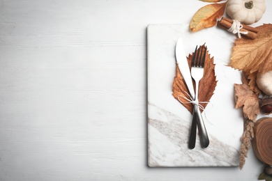 Photo of Cutlery, dry leaves and marble board on white wooden background, flat lay with space for text. Table setting elements