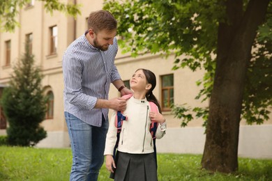 Photo of Father helping little daughter to put on school bag outdoors