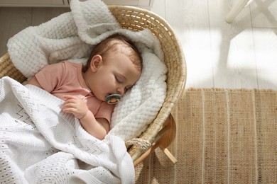 Photo of Cute little baby with pacifier sleeping in wicker crib at home, top view. Space for text