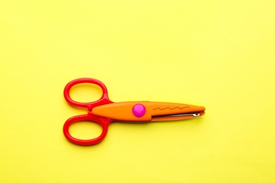 Decorative edge scissors on color background, top view