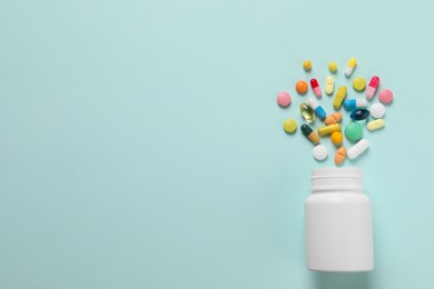 Photo of Plastic bottle with many different pills on light blue background, flat lay. Space for text